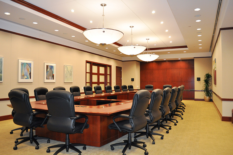 View of the traditionally appointed board room featuring dark stained wood trim and accents, high back leather seating, with fully integrated technology