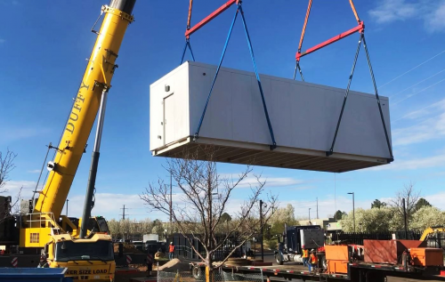 Prefabricated modular data center container suspended mid-air during crane pick into data center structure